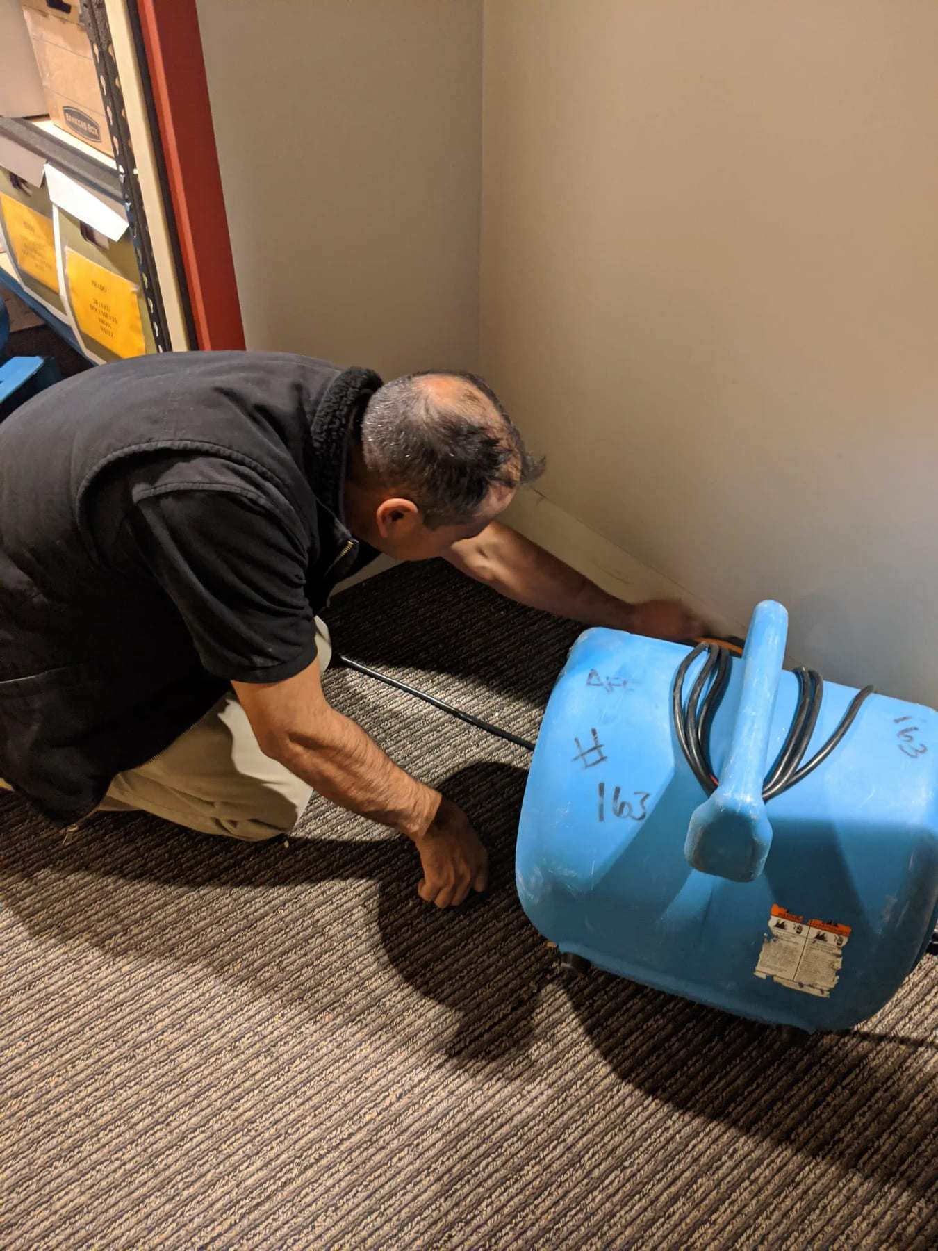 Technician kneeling to set an air mover at the edge of a wet carpet