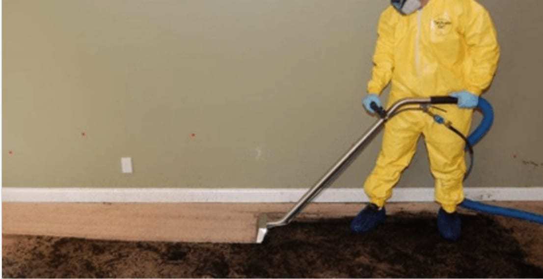 Technician in a protective suit extracting water from a soaked carpet